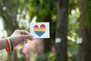 Herz Regenbogen Farben Karte halten im Hand welche hat Regenbogen Armband um Es, Konzept zum geben Liebe und einladend alle Menschen zu feiern lgbt Veranstaltungen im Stolz Monat. foto