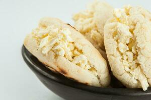 kolumbianisch traditionell Weiß Mais Arepa ausgestopft mit gerieben Käse im ein schwarz Keramik Gericht auf Weiß Hintergrund foto