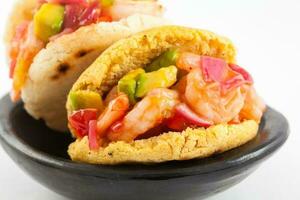 Arepas gefüllt mit Garnele Ceviche serviert im ein schwarz Keramik Gericht auf Weiß Hintergrund foto