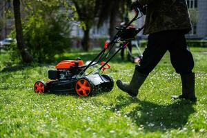 gemeinschaftlich Dienstleistungen Gärtner Arbeiter Mann mit Rasen Mäher zum Gras Schneiden im Stadt Park. foto