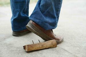 Nahansicht Mann trägt Schuhe ist Schritt auf rostig Metall Nagel auf Holz. Konzept, unsicher , Risiko zum gefährlich Tetanus. Sein Vorsichtig und aussehen um während Gehen beim Konstruktion Seite? ˅ oder Risiko setzt. foto