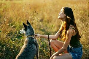 ein Frau sitzt Nächster zu ihr Hund Freund heiser im ein Feld von Gras und hält das Hund auf ein Leine während suchen beim das Sonnenuntergang von das Herbst Sonne foto