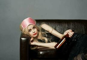 ein Frau Lügen mit ein Rosa Maske auf ihr Kopf und ein Flasche von Bier im ihr Hand auf das Couch foto