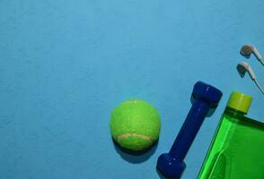 Blau Hantel, Grün Tennis Ball, und Flasche Anzeige trainieren planen auf Blau Hintergrund. oben Aussicht mit Kopieren Raum zum irgendein Design. gesund und Fitness Konzept foto