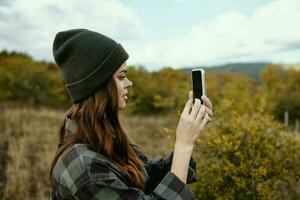 Frau mit Handy, Mobiltelefon Telefon im das Herbst Wald und Berge im das Hintergrund foto