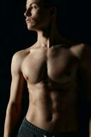 sexy Bodybuilder mit nackt Torso auf schwarz Hintergrund suchen zu das Seite abgeschnitten Aussicht foto