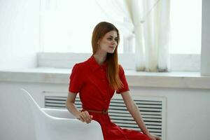 ziemlich Frau im rot Kleid Sitzung in der Nähe von das Fenster Mode foto