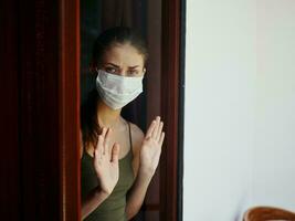 Frau im medizinisch Maske suchen aus das Fenster Quarantäne Verbot foto