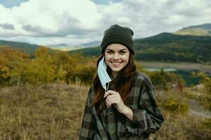 glücklich Frau im warm Kappen mit ein medizinisch Maske auf ihr Gesicht im das Wald im Natur foto