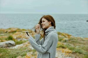 Frau im ein grau Sweatshirt mit ein Telefon im ihr Hände durch das Ozean foto