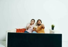 ein Mann und ein Frau sind Sitzung auf das Couch im Vorderseite von das Fernseher und ein Grün Blume im ein Topf drinnen foto