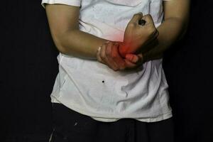 asiatisch Mann halten seine Hand. er fühlt sich Schmerzen auf seine Handgelenk mit schwarz Hintergrund. medizinisch oder Gesundheitswesen Konzept foto