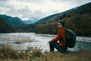 Frau in der Nähe von das Fluss im das Berge mit ein Rucksack auf ihr Schultern sind ruhen im das Herbst Wald foto