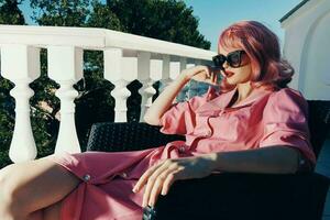schön Frau im Sonnenbrille draußen Sitzung auf das Terrasse entspannend unverändert foto