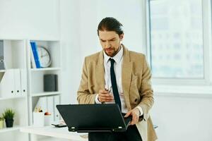 Mann im Beige Jacke im das Büro mit ein Laptop Exekutive foto