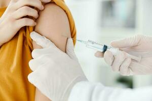 Arzt spritzt ein Impfstoff in das Schulter von ein weiblich geduldig im ein medizinisch Maske im ein Krankenhaus Seite Aussicht foto