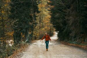 glücklich Reise mit ein Rucksack im ein warm Pullover, Hose und Stiefel Spaziergänge entlang das Straße im das Herbst Wald foto