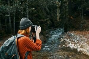 Frau mit ein Kamera auf Natur im das Berge in der Nähe von das Fluss Seite Aussicht foto