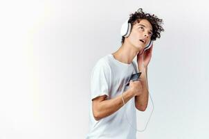 Mann mit lockig Haar im Weiß T-Shirt Hören zu Musik- mit Kopfhörer Telefon Technologie foto