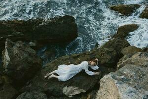attraktiv Frau mit lange Haar im ein abgelegen Stelle auf ein wild felsig Küste im ein Weiß Kleid unverändert foto