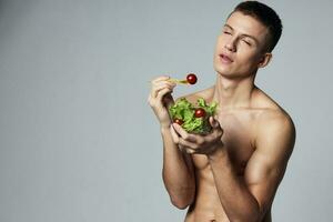 ein Mann mit ein gepumpt oben Körper ein Teller von Salat Essen Gemüse Bodybuilder foto