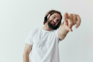 glücklich Mann Hören zu Musik- und lächelnd im ein Weiß T-Shirt auf ein Weiß Hintergrund und zeigen ein Finger beim das Bildschirm beim das Kamera foto