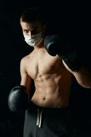 Athlet Boxen Handschuhe auf ein schwarz Hintergrund medizinisch Maske auf das Gesicht foto