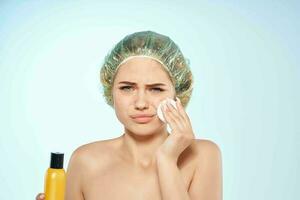 verärgert Frau abwischen ihr Gesicht mit ein aufladen Rabatt Haut Pflege Lotion Blau Hintergrund foto