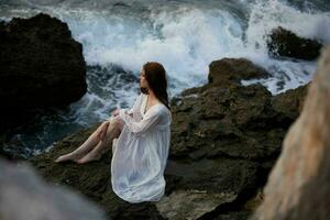 barfuß Frau im Weiß Kleid sitzt auf ein Cliff Natur oben Aussicht foto