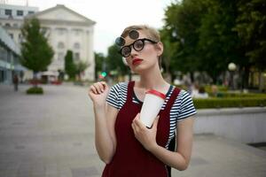 Frau mit kurz Haar auf das Straße tragen Brille Glas mit trinken gehen foto