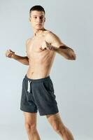 Athlet im kurze Hose Gesten mit seine Hände auf ein grau Hintergrund und Bodybuilder trainieren foto