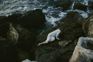 Frau im ein abgelegen Stelle auf ein wild felsig Küste im ein Weiß Kleid unverändert foto