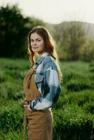 ein Frau Gärtner im ein Schürze steht im ein Feld von Grün Gras draußen, lächelnd auf ein Sommer- Tag in ein Sonnenuntergang foto