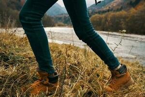 Damen Füße Jeans Schuhe trocken Gras Herbst Fluss Berge im das Entfernung foto