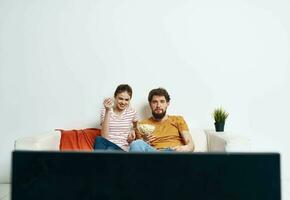 ein Mann und ein Frau sind Sitzung auf das Couch im Vorderseite von das Fernseher und ein Grün Blume im ein Topf drinnen foto