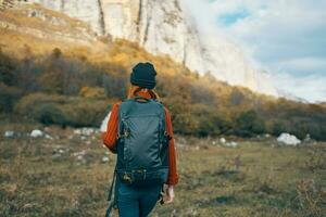 Frau im ein warm Hut mit ein Rucksack auf ihr zurück und im ein Sweatshirt draußen im das Berge gestikulieren mit ihr Hände foto