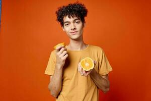 lockig Kerl im ein Gelb T-Shirt Orangen im seine Hände rot Hintergrund foto