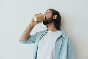 freiberuflich tausendjährig Mann mit Bart Trinken Kaffee von ein Krabbe Tasse im stilvoll Hipster Kleider auf ein Weiß Hintergrund foto