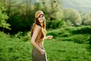 ein jung Frau mit ein sportlich Körper Spaziergänge im ein Sommer- Grün Park im Natur. Sonnenuntergang Sonnenlicht leuchtet ihr rot Haar foto