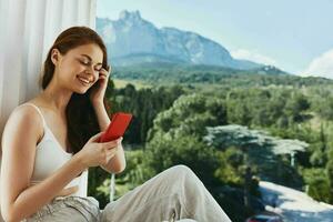 attraktiv jung Frau mit ein rot Telefon Terrasse draussen Luxus Landschaft Freizeit unverändert foto