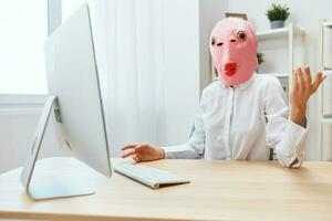 komisch verrückt Geschäftsfrau Arbeiter Freiberufler im Rosa Fisch Maske Arbeit auf Computer online Nachdenken oder Herstellung Entscheidung schockiert durch betriebsbereit Probleme erziehen Hand oben im Licht modern Büro. Kopieren Raum foto