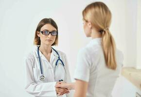 Arzt im ein medizinisch Kleid mit ein Stethoskop und ein geduldig im ein Weiß T-Shirt zurück Aussicht foto