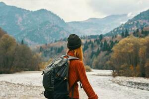 Frau Wanderer mit ein Rucksack sich ausruhen im das Berge im Natur in der Nähe von das Fluss foto