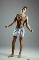 männlich Bodybuilder im kurze Hose gestikulieren mit seine Hände auf grau Hintergrund voll Wachstum drinnen foto