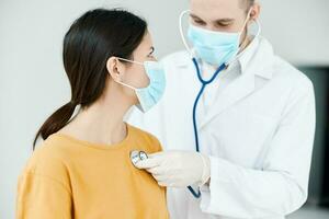 Arzt mit Stethoskop hört zu zu Herzschlag von geduldig tragen medizinisch Maske im Krankenhaus foto