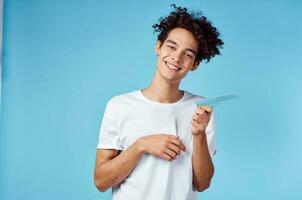 glücklich Kerl mit ein Kamm im seine Hand auf ein Blau Hintergrund und lockig Haar Brünette Modell- foto