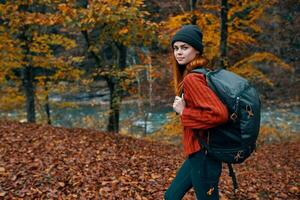 gefallen Blätter im das Park im Herbst und das Fluss im das Hintergrund Frau Tourist mit ein Rucksack Reise foto