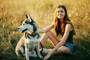 Frau ruhen nach ein gehen sitzt im ein Feld mit ein Dackel Hund lächelnd während Ausgaben Zeit draußen mit ein Freund Hund im Herbst beim Sonnenuntergang während Reise foto