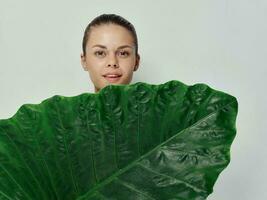 ziemlich Frau Abdeckungen ihr Körper mit Grün Blatt Lächeln Licht Hintergrund foto