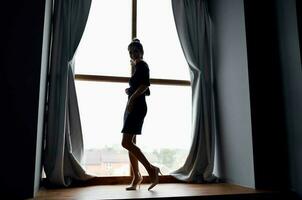 Frau in der Nähe von das Fenster im schwarz Kleid und posieren foto